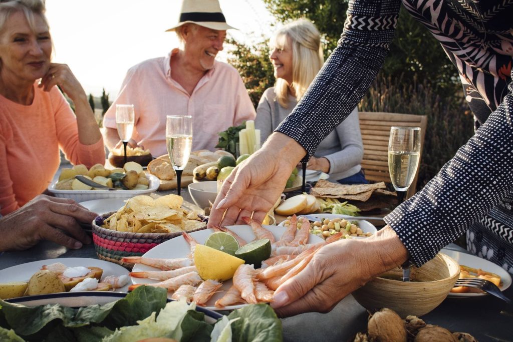 Senioren sitzen beim Essen an einem bunt gedeckten Tisch in einer mediterranen Umgebung
